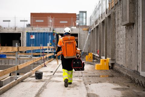HLM-landmåler på vej ind på byggepladsen med instrumentrygsæk og værktøjstaske