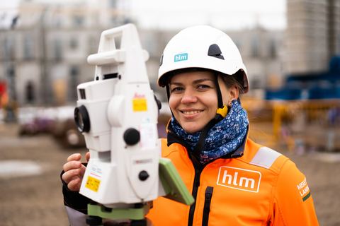 Smilende HLM-landmåler med totalstation på byggepladsen