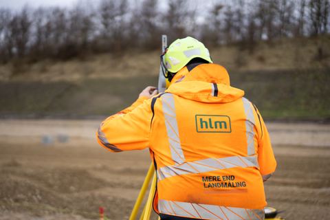 HLM-landmåler i HLM-jakke ved måleinstrumentet på et jordarbejde